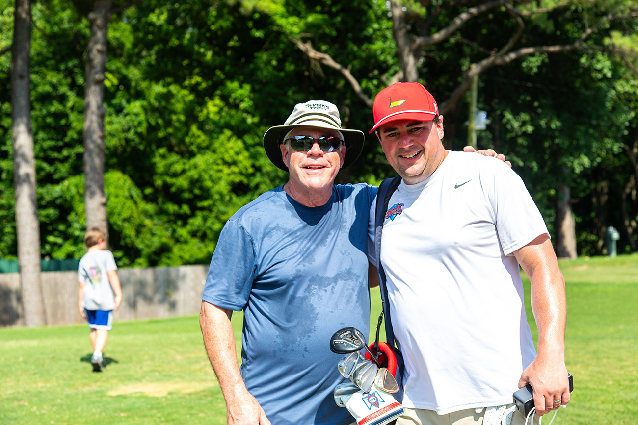 A golfer and his dad pose for a photo on the first tee